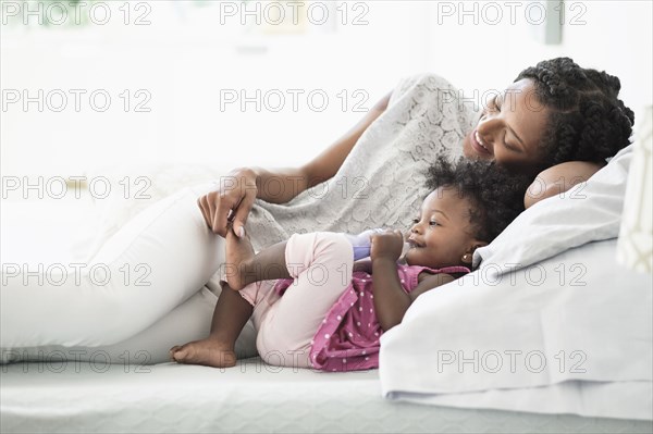 Black woman playing with foot of baby daughter on bed