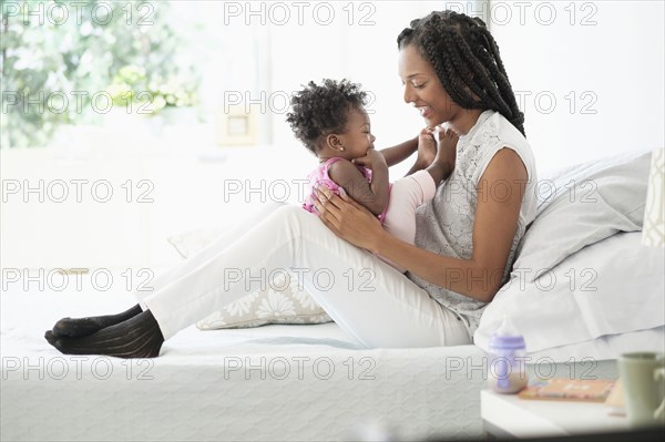 Black woman cuddling with baby daughter on bed