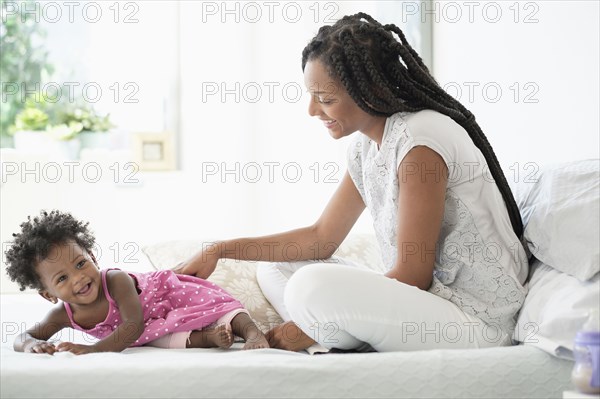 Black woman playing with baby daughter on bed