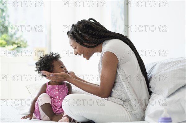 Black woman cupping face of baby daughter on bed