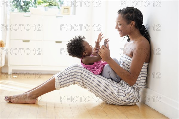 Black woman sitting on floor clapping hands with baby daughter