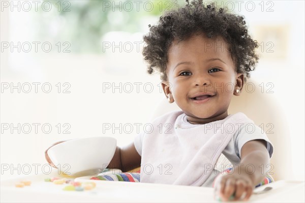 Smiling Black baby girl eating cereal from bowl in high chair