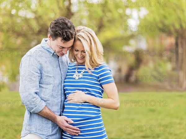 Smiling Caucasian man and expectant mother looking at belly