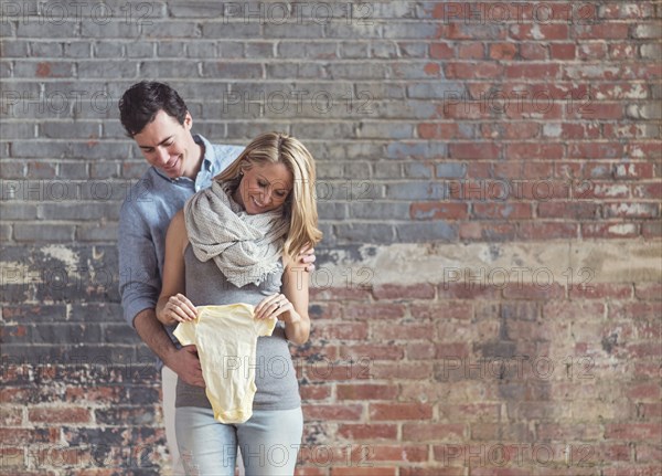 Smiling Caucasian man and expectant mother holding onesie