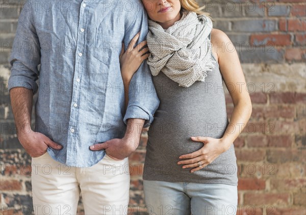 Smiling Caucasian expectant mother holding arm of man