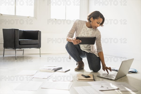 Black businesswoman using laptop and digital tablet on floor