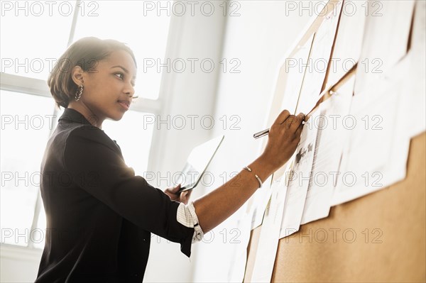 Black businesswoman using digital tablet writing on paperwork