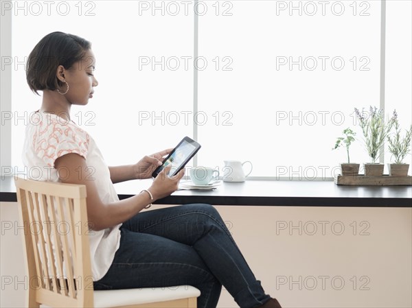 Black woman using digital tablet at coffee shop near window