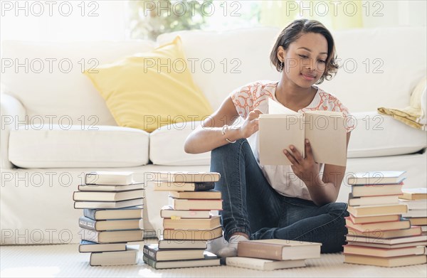 Black woman sitting on floor reading pile of books