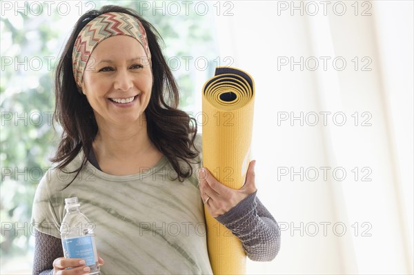 Smiling Hispanic woman holding exercise mat and water bottle