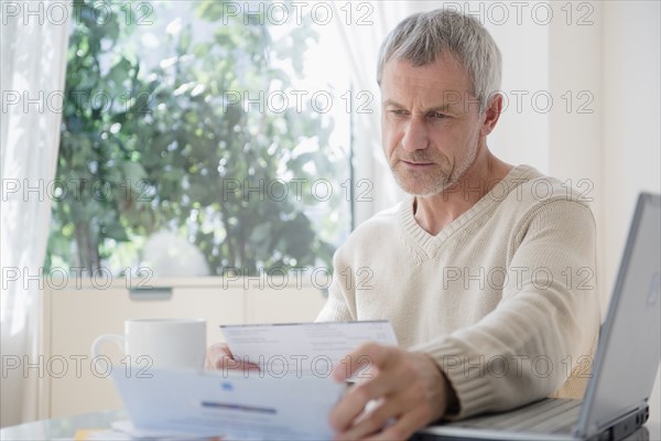 Older Caucasian man paying bills using laptop