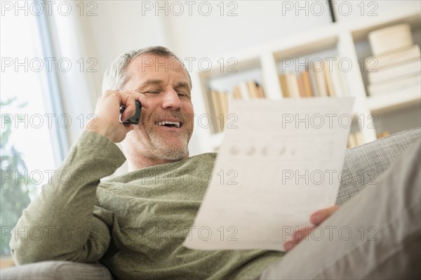 Older Caucasian man talking on telephone reading paperwork