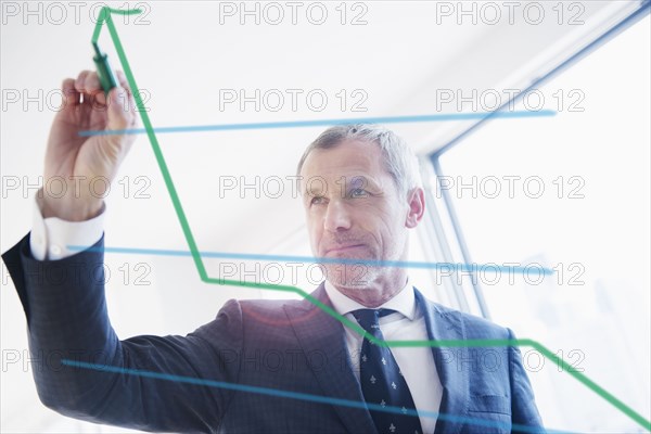 Older Caucasian businessman drawing chart on glass wall