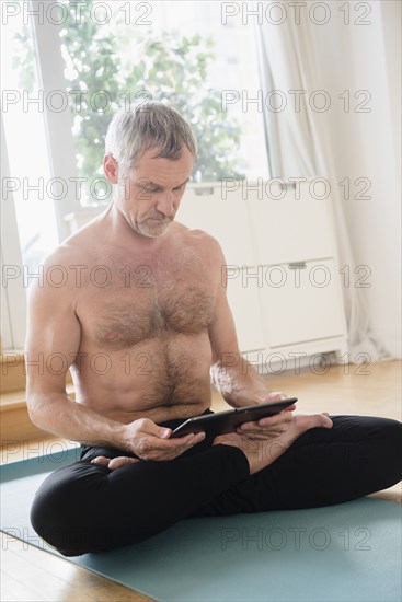 Older Caucasian man using digital tablet on exercise mat