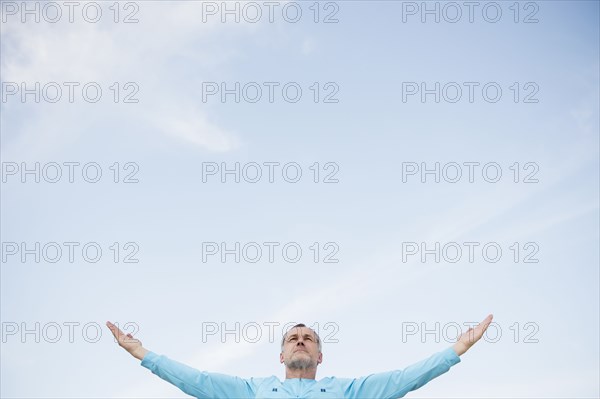 Older Caucasian man with arms outstretched against blue sky