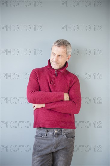 Older Caucasian man wearing sweater leaning on wall