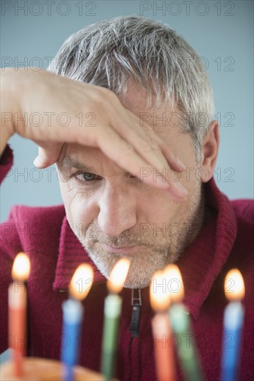 Older Caucasian man frowning at birthday cake