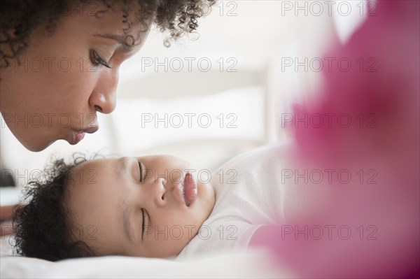 Mother kissing baby son sleeping on bed
