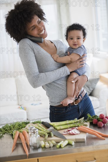 Mother talking on telephone while holding baby son in kitchen