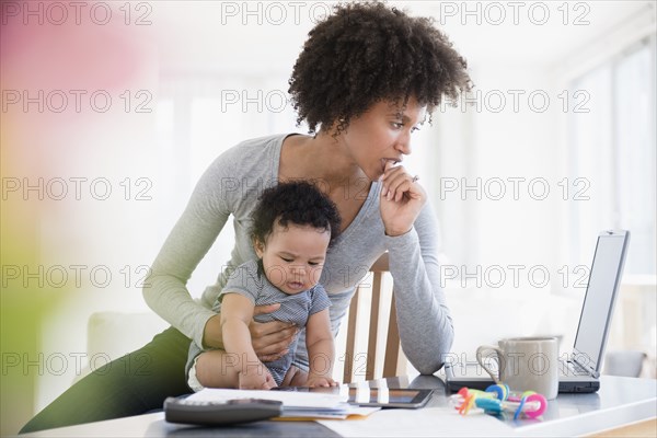 Mother holding baby son worrying about laptop