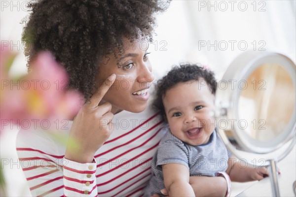 Mother holding baby son applying face cream in mirror