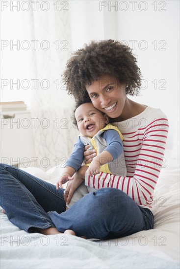 Smiling mother holding baby son on bed