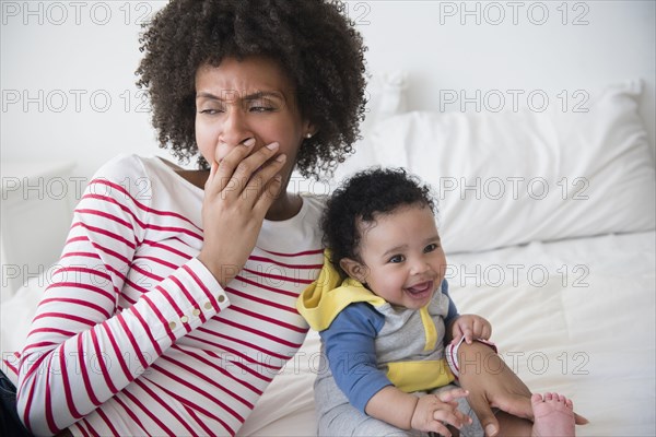 Mother yawning on bed holding baby son