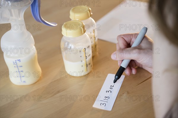 Caucasian woman writing date and volume for breast milk bottles