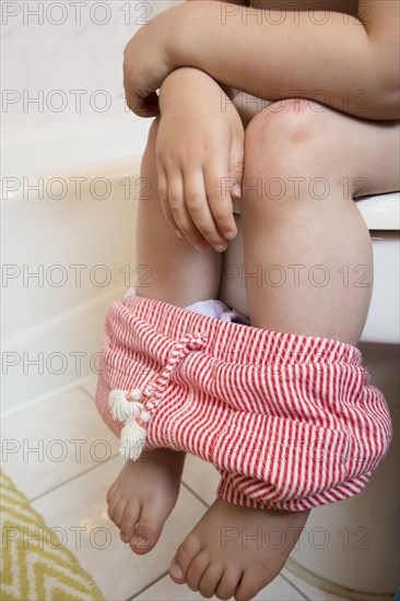 Legs of Caucasian girl sitting on toilet