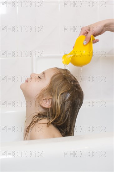 Caucasian mother rinsing hair of daughter in bathtub