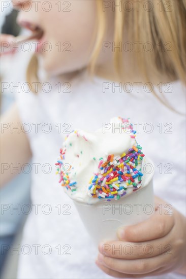 Caucasian girl eating cup of ice cream with sprinkles