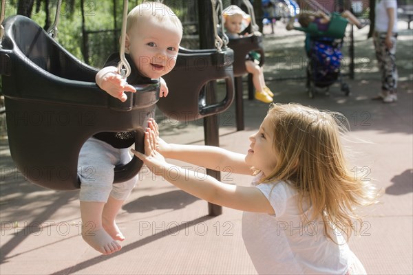 Caucasian girl pushing baby in swing