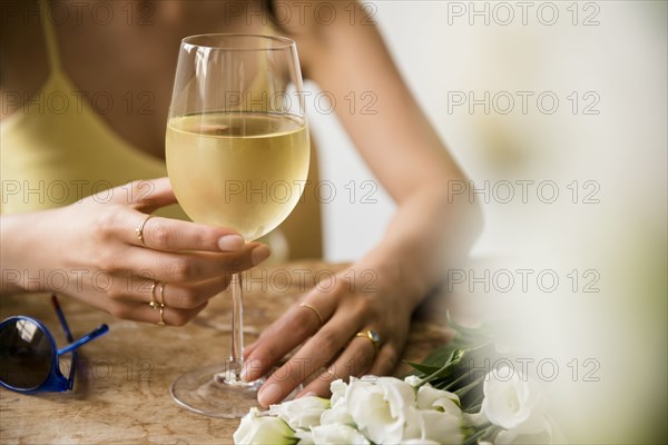 Hispanic woman drinking wine near flowers and sunglasses