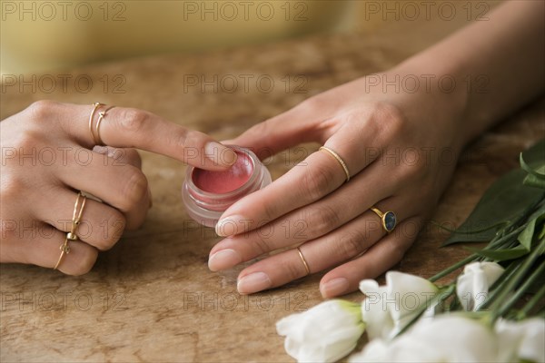 Hands of Hispanic woman holding jar of lip gloss