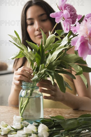 Hispanic woman arranging pink flowers in jar