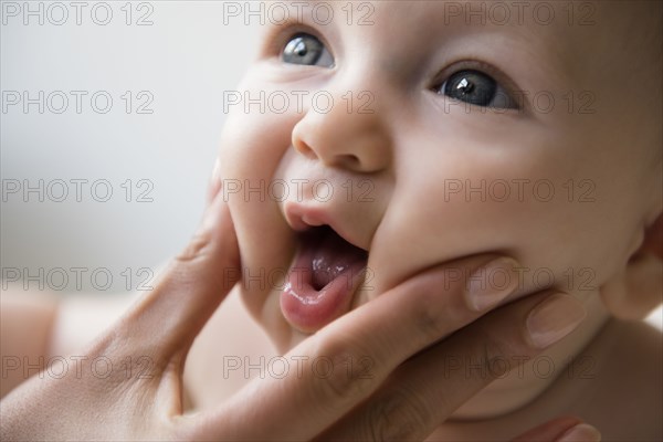 Hand of mother squeezing cheeks of baby son