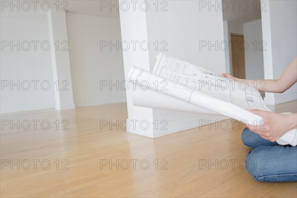 Hispanic woman sitting on floor of empty apartment holding blueprint