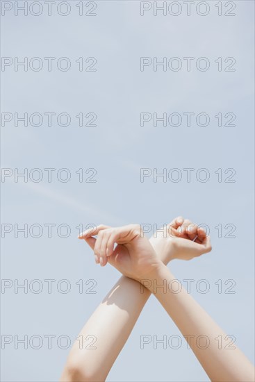 Hispanic woman crossing arms at wrist under blue sky