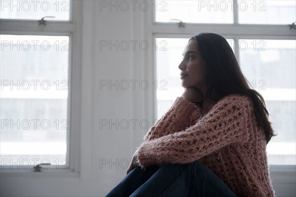 Hispanic woman wearing pink sweater and jeans near window