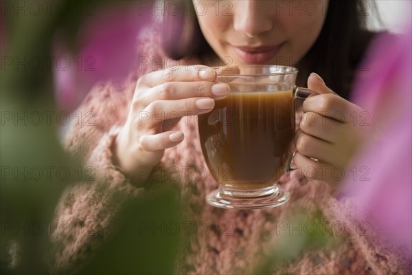 Hispanic woman drinking coffee behind flowers