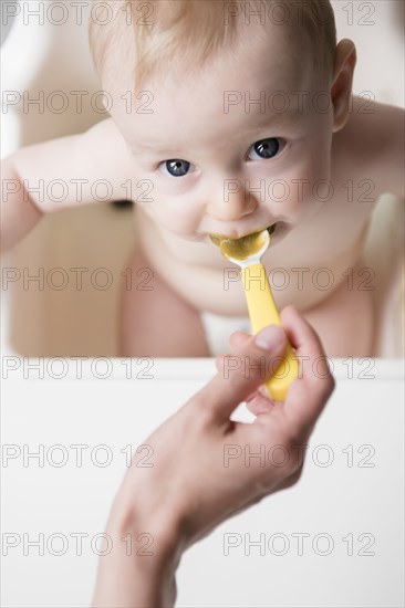 Caucasian mother feeding baby son with spoon in high chair