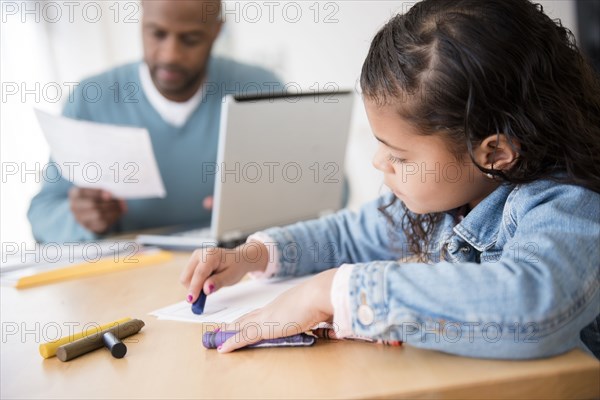 Daughter coloring with crayons while father uses laptop