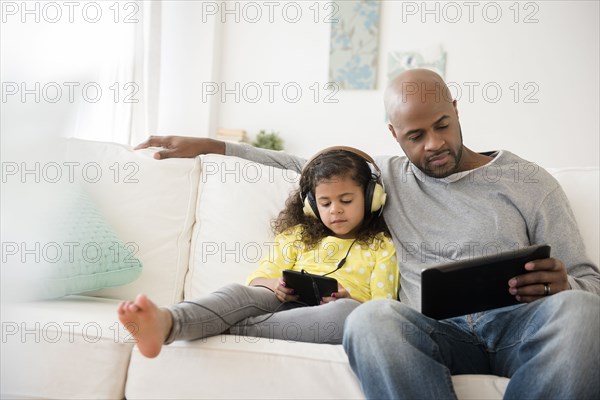 Father and daughter using digital tablets on sofa