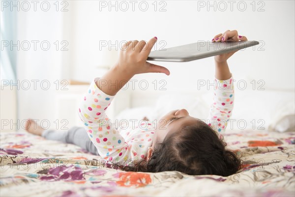 Mixed Race girl laying on bed using digital tablet