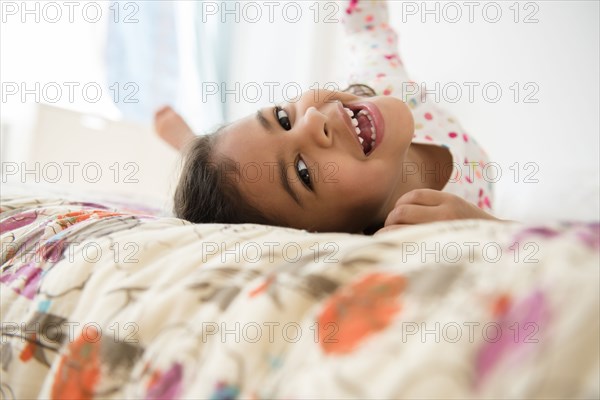 Smiling Mixed Race girl rolling on bed