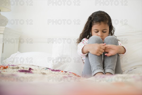 Unhappy Mixed Race girl sitting on bed