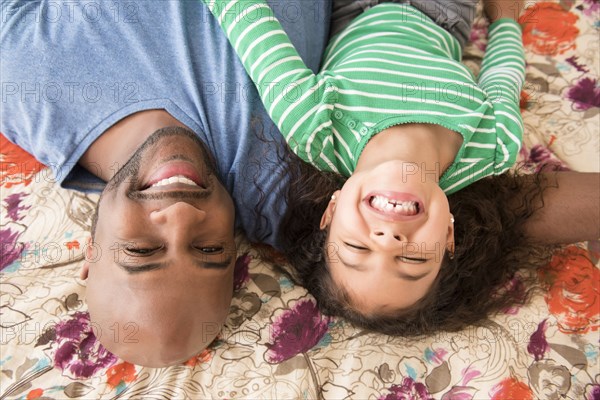 Smiling father and daughter laying on bed