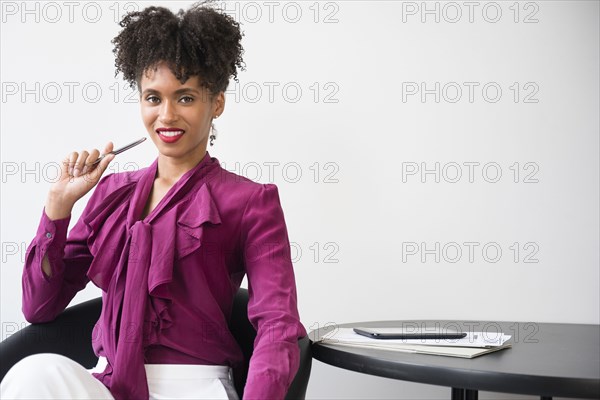 Smiling Black woman wearing purple blouse holding pen