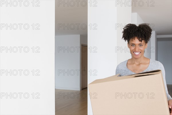 Black woman carrying cardboard box in empty apartment