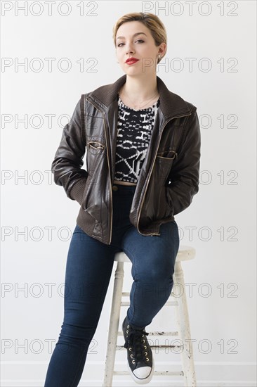 Caucasian woman wearing leather jacket sitting on stool